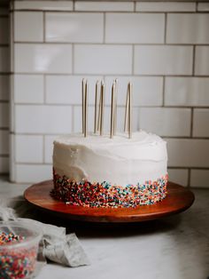 a white cake with sprinkles and candles on it sitting on a plate