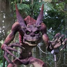 an animated creature with green eyes and large horns standing in front of a forest filled with trees