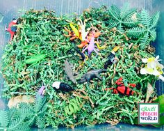 a plastic container filled with different types of toy figurines on top of green plants