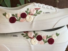 two pairs of white shoes with red and pink flowers painted on the side of them