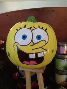 a yellow pumpkin with a face painted on it sitting on a wooden stand next to other items