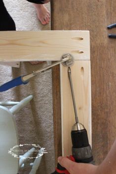 a person is using a drill to fix a piece of wood on the floor next to a chair