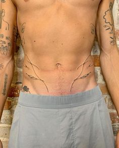 a man with tattoos on his chest standing in front of a brick wall