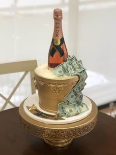 a cake with money on top and a bottle of champagne in the middle sitting on a table