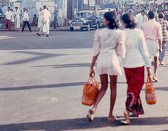 two women are walking down the street with bags in their hands and one woman is holding an orange purse