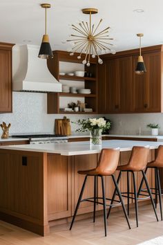 a kitchen with wooden cabinets and white marble counter tops, four bar stools in front of the island