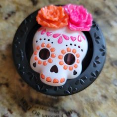 a white and orange sugar skull with pink flowers on it's head sitting on a counter