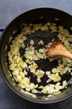 onions being cooked in a pot with a wooden spoon