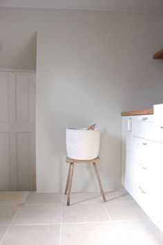 a white basket sitting on top of a wooden stand in a room with tile flooring