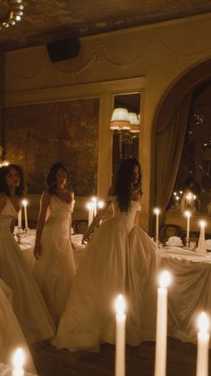 two women in white dresses standing next to candles