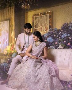 a man and woman sitting next to each other on a couch in front of flowers