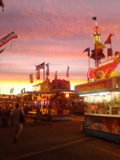 an amusement park at dusk with people walking around and rides on the carousel in the foreground