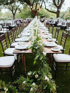 a long table is set up with white linens and greenery for an outdoor wedding