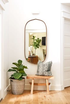 a wooden bench sitting under a mirror next to a plant in a pot on top of a hard wood floor