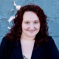 a woman with curly red hair smiling at the camera while standing in front of a blue wall