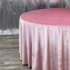 a round table with a pink cloth on it in front of a glitter wall and wooden floor