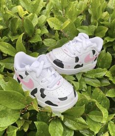 a pair of white and pink shoes sitting on top of green leaves in the grass