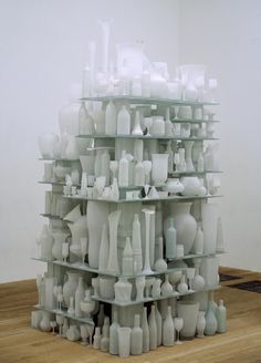 a large stack of white vases sitting on top of a wooden floor next to a wall