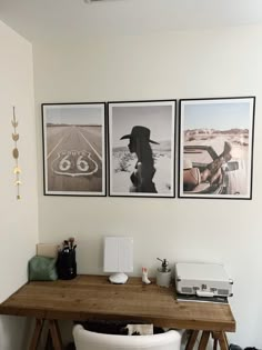 three pictures hang on the wall above a wooden table with two chairs and a typewriter