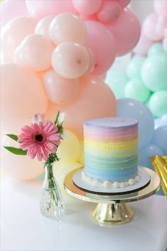 there is a cake on the table with balloons in the back ground and a pink flower next to it