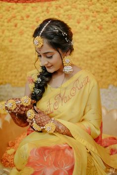 a woman in yellow sari sitting down with her hands on her chest and holding flowers