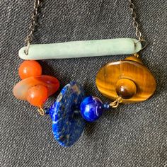 For your consideration: Handmade Modern Bar Necklace with Lapis, Carnelian, Tiger Eye bead and donut links on an antique jade bar.  It is hard to describe this necklace: 3 Saturn flying saucer type links consisting of 2 round and one donut shaped bead hang from an antique jade bar. The links are carnelian, lapis lazuli and tiger eye.  The necklace has an approximate 15" drop on a gunmetal color metal chain.  It has a modern yet primitive and spiritual look.  Please see pictures and dm me with questions. Artisan Gemstone Rondelle Necklace, Artisan Necklaces With Large Beads For Healing, Carnelian Necklaces With Large Beads, Unique Carnelian Necklaces With Large Beads, Unique Orange Gemstone Bead Necklaces, Unique Carnelian Beads Gems And Cabochons For Gift, Unique Carnelian Necklace With Natural Stones, Handmade Blue Carnelian Jewelry, Carnelian Amulet Necklace With Large Beads