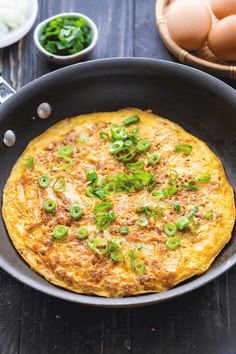 an omelet in a pan with green onions and eggs around it on a wooden table