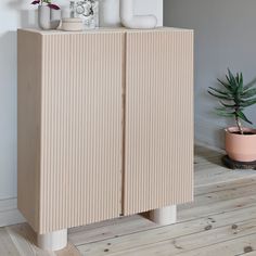 a cabinet with three vases on top of it next to a potted plant