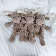 there are four stuffed animals laying together on the white bed sheet, one is crocheted and the other is made out of yarn