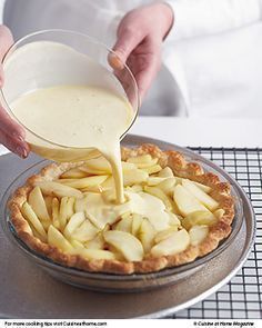 a person pouring milk into a pie on top of a metal pan covered in apples