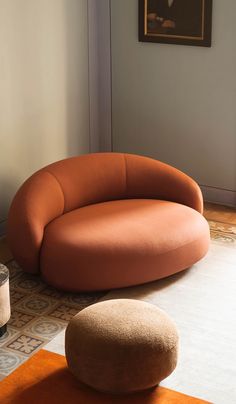 an orange couch sitting on top of a rug next to a round footstool