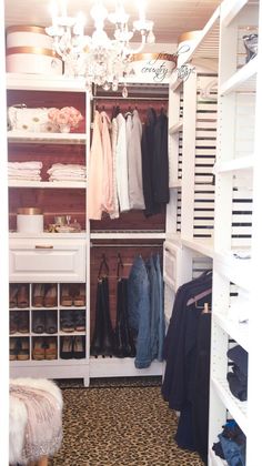 an organized closet with clothes, shoes and coats hanging on shelving units in front of a chandelier