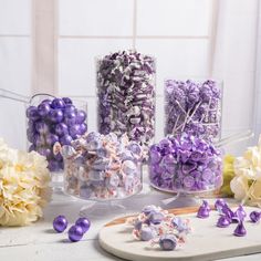 purple and white candies are arranged in glass vases on a table with flowers