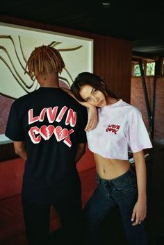 a man and woman standing next to each other in front of a wall with graffiti on it