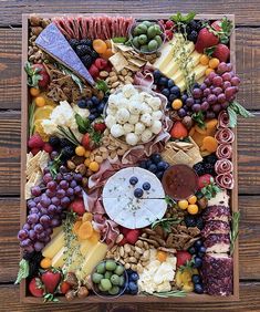 an assortment of cheeses, fruits and meats arranged in a square wooden box