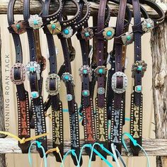 a bunch of different colored belts hanging on a wooden rack with turquoise beads and stones