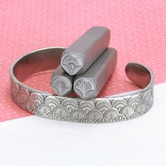 two silver bracelets sitting next to each other on a pink and white tablecloth