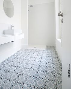 a bathroom with blue and white tile flooring next to a shower stall, sink and mirror