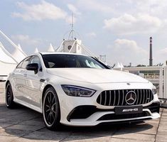 a white mercedes cla is parked in front of a fenced area with tents