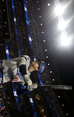 a baseball player is jumping in the air with his bat and helmet on, while lights shine behind him