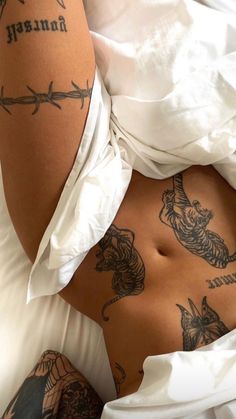 a woman laying in bed with tattoos on her stomach and arms behind her back, looking down at the camera