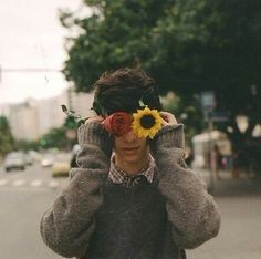 a man with a sunflower in his hair is covering his eyes while walking down the street