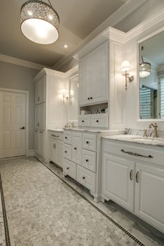 a large bathroom with two sinks, mirrors and lights on the ceiling above it is also white cabinetry