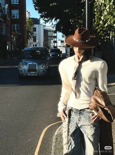 a man wearing a cowboy hat and tie standing on the side of a road with his hands in his pockets