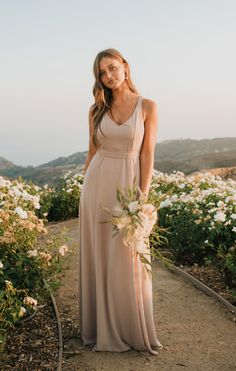 a woman in a long dress standing on a path with white flowers and greenery