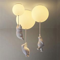 three white lamps hanging from the ceiling with bears and balls attached to each lamp fixture