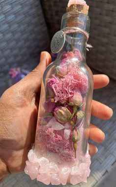 a person holding a bottle filled with pink flowers and leaves in it's hand