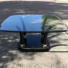 a glass table sitting on top of a parking lot next to a tree and sidewalk