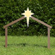 a wooden nativity set with a star on top in the middle of some grass