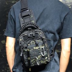 a man wearing a black t - shirt with a camouflage bag on his back, standing in front of a wall